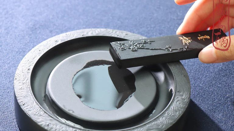 Bàn tay cầm thỏi mực đen phía trên nghiên tròn có mực